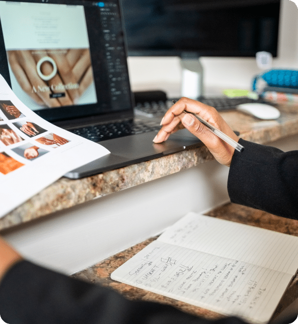 A person working on a turnkey website on a laptop with a hand image, papers with hand images, and a notepad with notes.